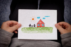 Child holds a drawn house with family. Close up.