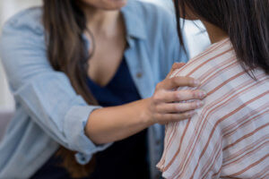 A close up photo of a mom comforting her daughter by putting her hand on her daughter's shoulder.