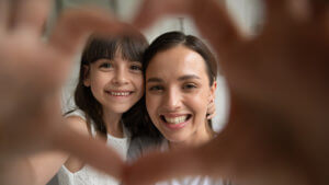 Close up head shot portrait happy family of two making heart gesture, focus on smiling young mother bonding little cute daughter. Overjoyed small girl showing love sign with millennial mommy.